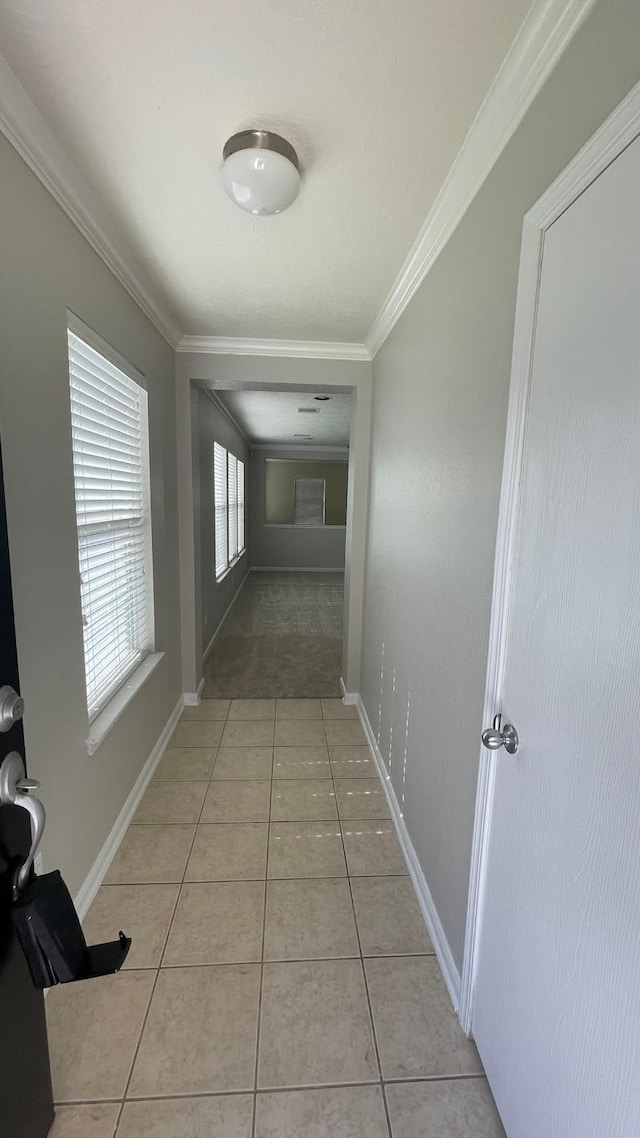 corridor featuring baseboards, light tile patterned flooring, and crown molding