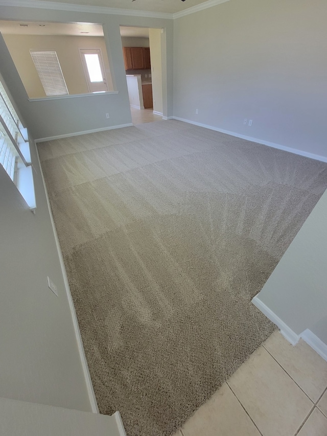 unfurnished room featuring light carpet, ornamental molding, baseboards, and light tile patterned flooring