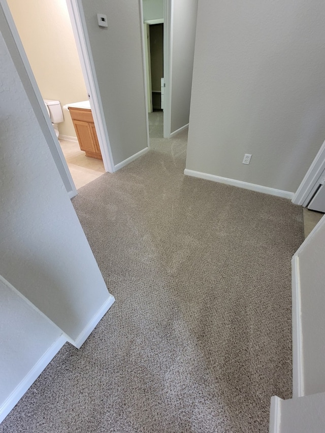 interior space featuring light carpet, ensuite bath, and baseboards