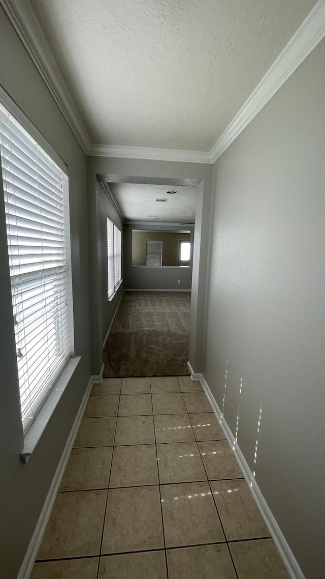 hallway featuring tile patterned flooring, a textured ceiling, crown molding, and baseboards