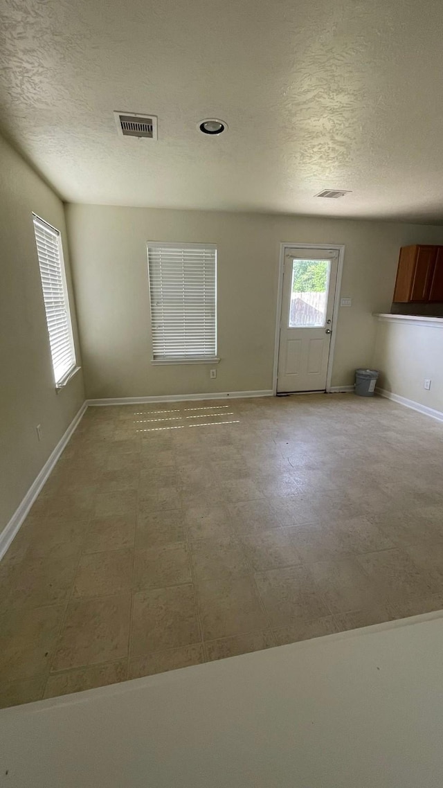 unfurnished room featuring visible vents, a textured ceiling, and baseboards