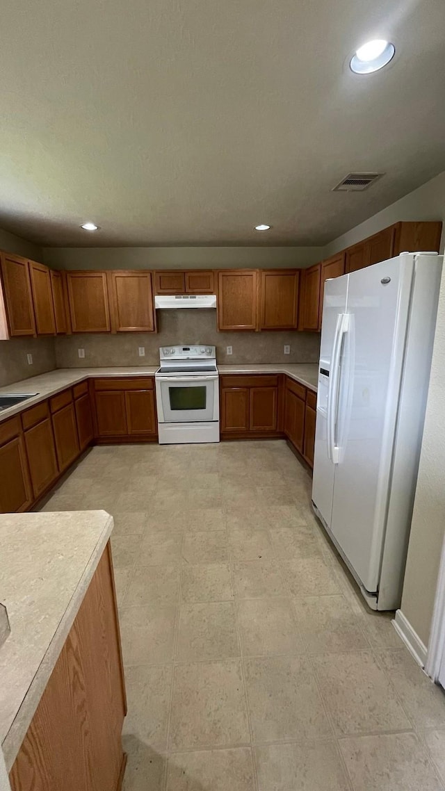 kitchen featuring white appliances, visible vents, light countertops, under cabinet range hood, and brown cabinets