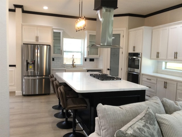 kitchen with glass insert cabinets, ornamental molding, island range hood, stainless steel appliances, and a sink