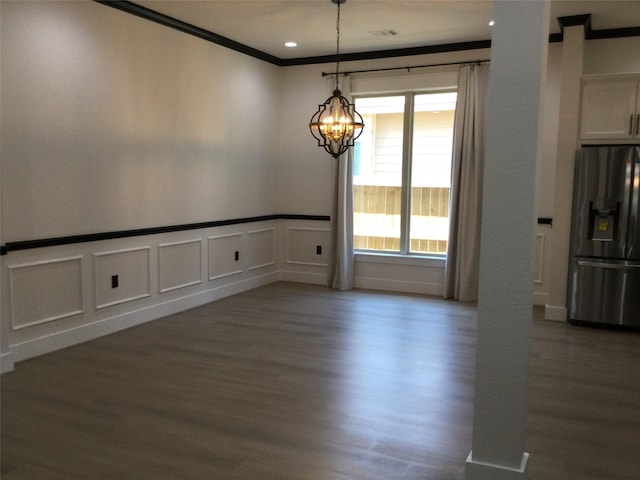 unfurnished dining area with visible vents, wood finished floors, an inviting chandelier, crown molding, and a decorative wall