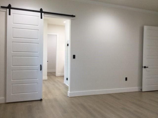 unfurnished room featuring crown molding, baseboards, light wood-type flooring, and a barn door