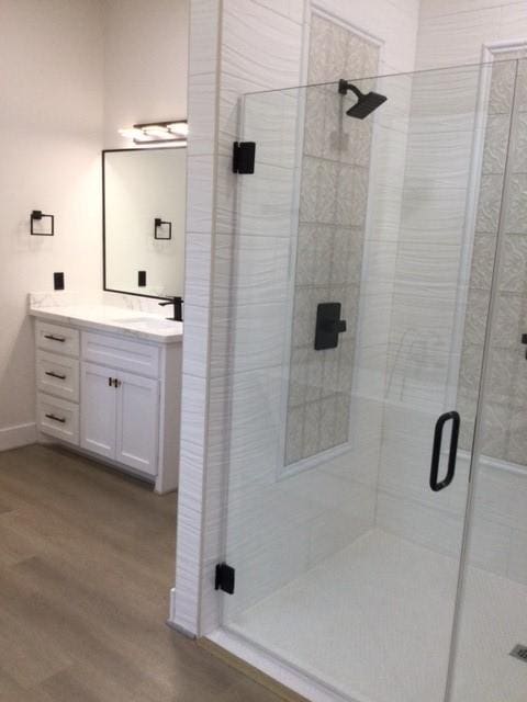 bathroom with vanity, a shower stall, wood finished floors, and baseboards