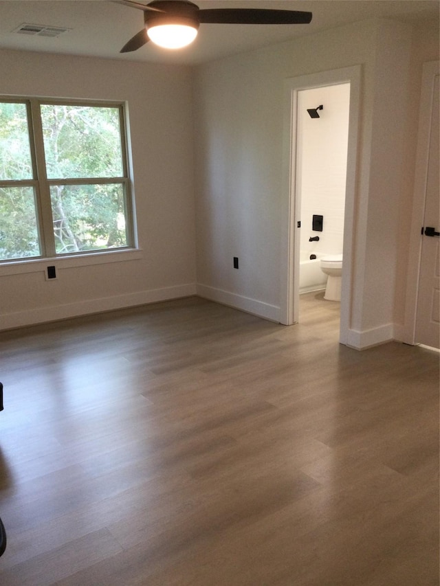 unfurnished room featuring a ceiling fan, visible vents, wood finished floors, and baseboards