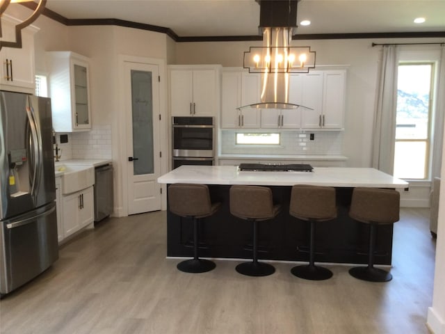 kitchen featuring light wood-type flooring, white cabinetry, appliances with stainless steel finishes, wall chimney exhaust hood, and light countertops