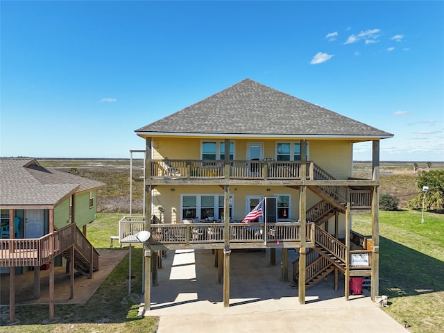 rear view of property featuring a yard, stairway, roof with shingles, and a deck