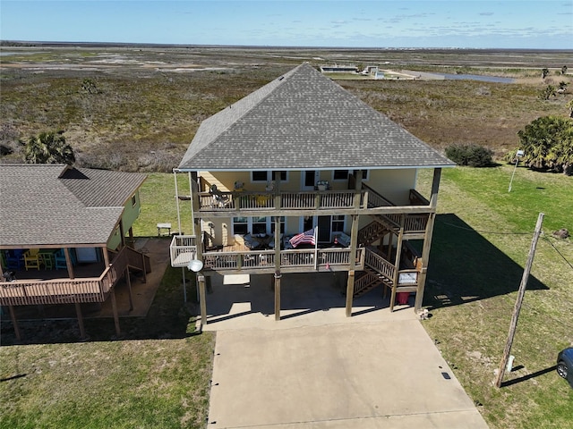 view of front facade with stairs, a front yard, roof with shingles, a deck, and a balcony