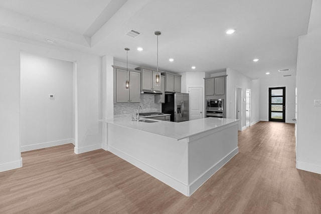 kitchen with backsplash, gray cabinetry, light countertops, appliances with stainless steel finishes, and a sink