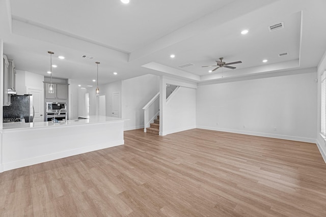 unfurnished living room featuring stairs, a tray ceiling, light wood-style flooring, and visible vents