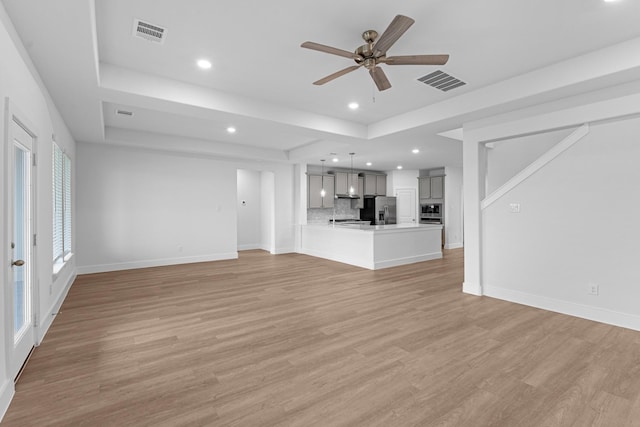 unfurnished living room with visible vents, light wood-style flooring, a raised ceiling, and baseboards