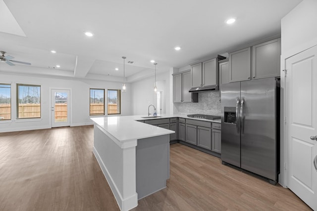 kitchen with gray cabinetry, a peninsula, stainless steel fridge, gas cooktop, and a sink