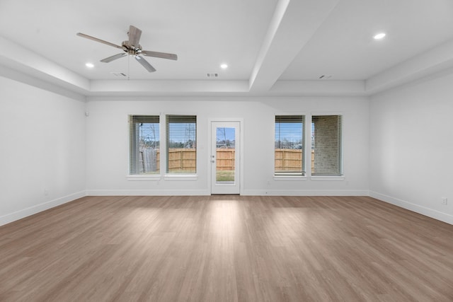 unfurnished room with a tray ceiling, baseboards, visible vents, and light wood finished floors