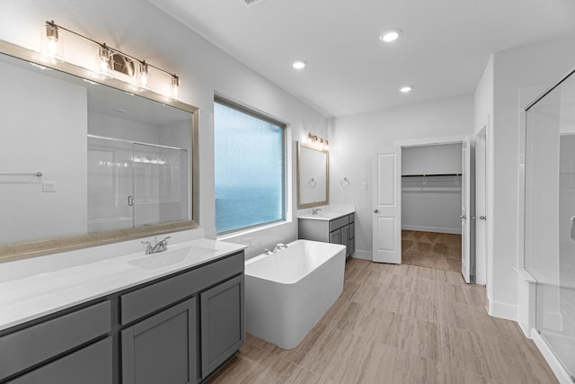 bathroom featuring a soaking tub, two vanities, recessed lighting, a stall shower, and a sink