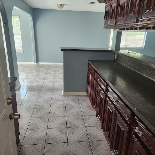 kitchen with dark countertops, light tile patterned floors, visible vents, and arched walkways