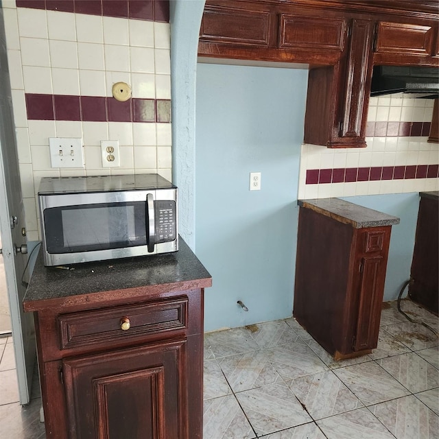 kitchen with stainless steel microwave, dark countertops, tasteful backsplash, and reddish brown cabinets