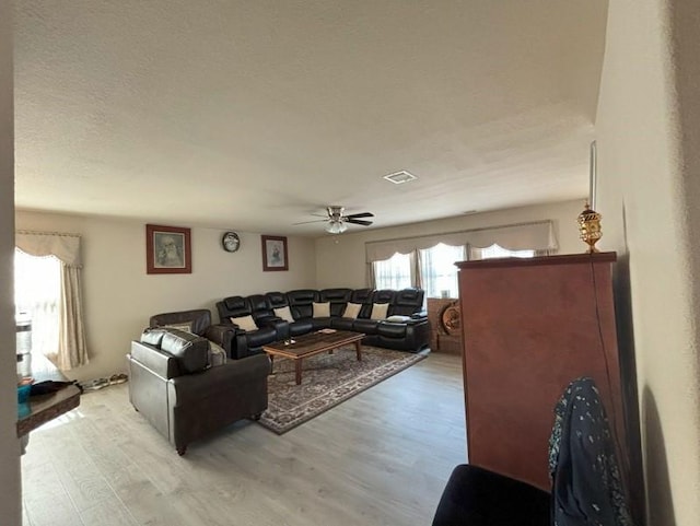 living area featuring a ceiling fan, visible vents, light wood finished floors, and a textured ceiling