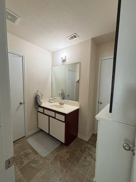 bathroom with visible vents, baseboards, a textured ceiling, and vanity