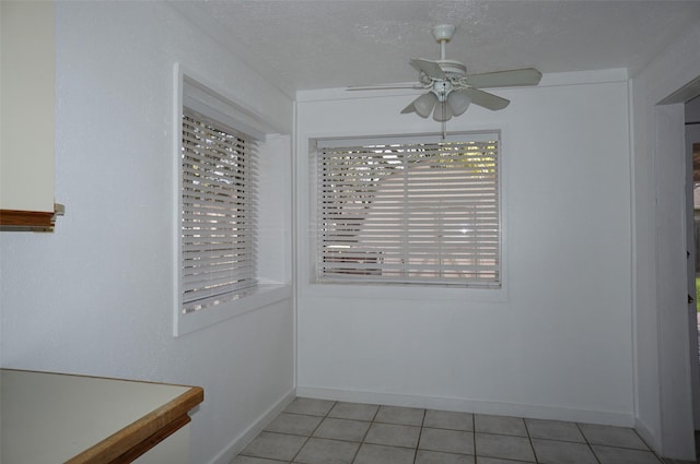 unfurnished dining area featuring light tile patterned flooring, a ceiling fan, and a textured ceiling