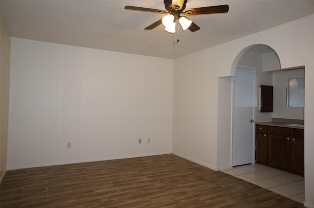 empty room featuring baseboards, light wood-type flooring, arched walkways, a ceiling fan, and a sink