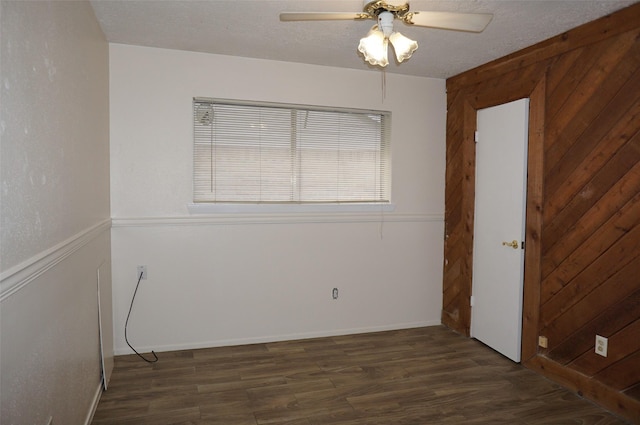 empty room with ceiling fan, wooden walls, wood finished floors, and a textured ceiling