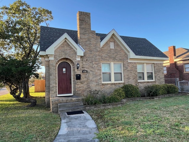 tudor house featuring a front yard, fence, and brick siding