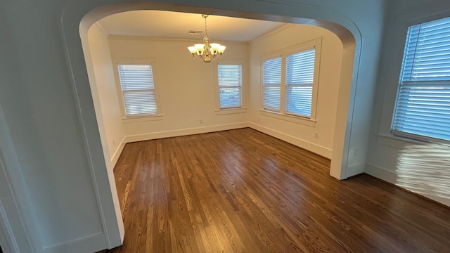 spare room featuring baseboards, dark wood-type flooring, a chandelier, and crown molding