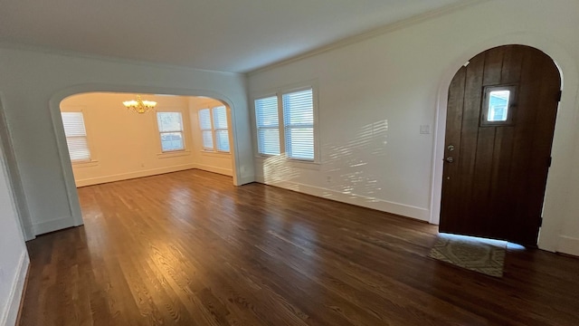 entrance foyer with a notable chandelier, dark wood-style floors, arched walkways, and ornamental molding