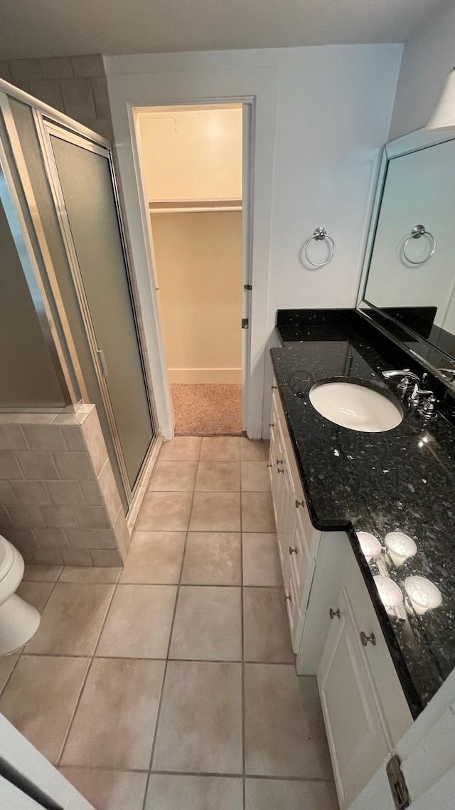 full bathroom with a walk in closet, vanity, a shower stall, and tile patterned flooring