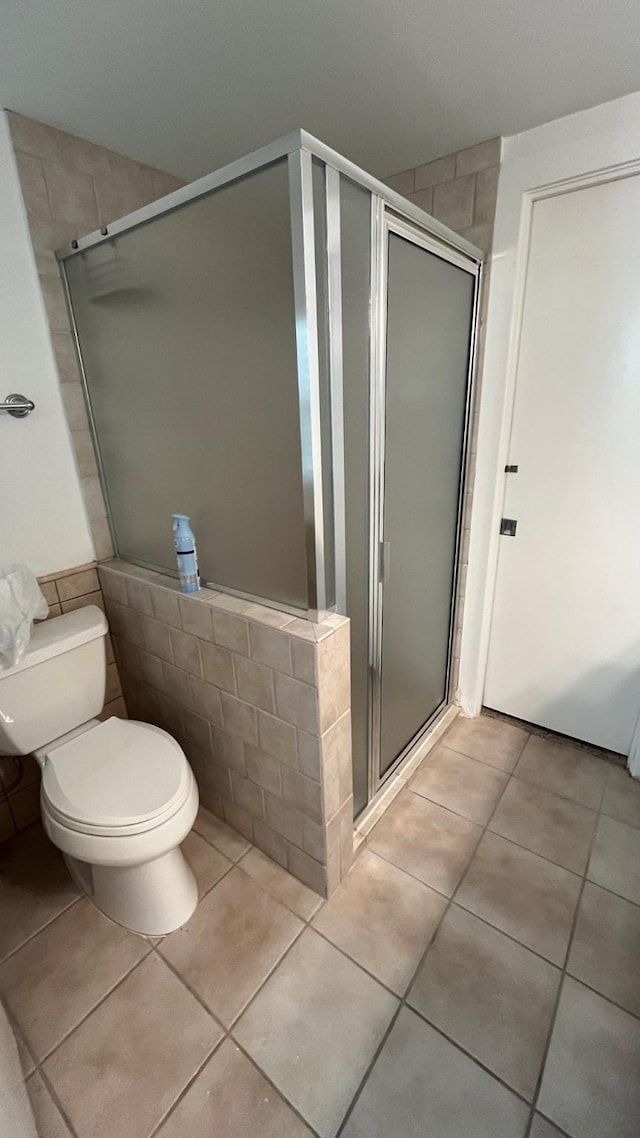 bathroom with tile patterned flooring, toilet, and a stall shower