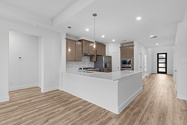 kitchen with tasteful backsplash, light countertops, appliances with stainless steel finishes, light wood-style floors, and a sink