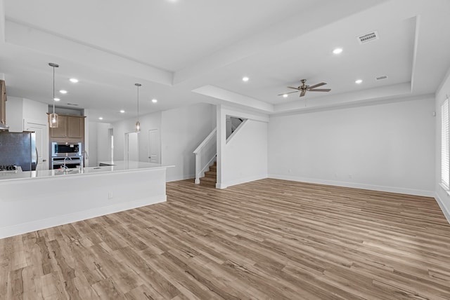 unfurnished living room with visible vents, light wood-style flooring, recessed lighting, a raised ceiling, and stairs