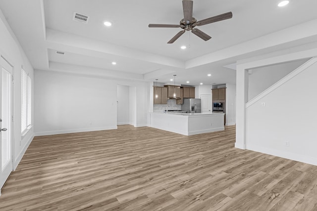 unfurnished living room featuring baseboards, visible vents, light wood finished floors, recessed lighting, and a raised ceiling