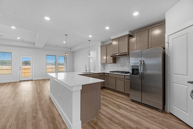 kitchen with light wood-type flooring, a peninsula, stainless steel fridge, gas cooktop, and a sink