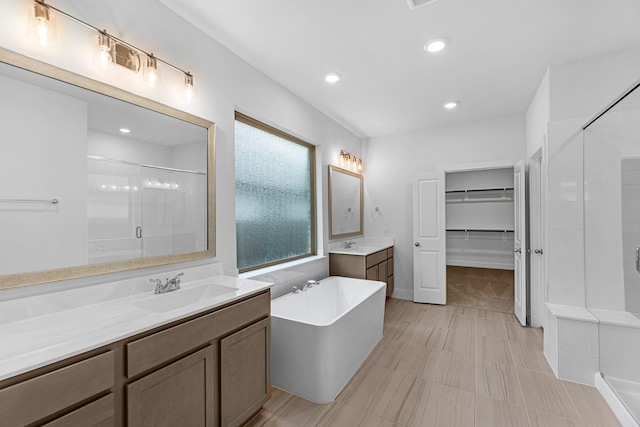 bathroom with recessed lighting, a soaking tub, a shower stall, and a sink