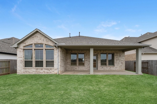 back of property featuring brick siding, a shingled roof, a lawn, a fenced backyard, and a patio area