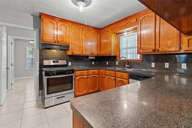 kitchen featuring backsplash, under cabinet range hood, gas range, light tile patterned floors, and a sink