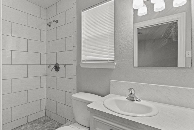 full bath with toilet, tiled shower, vanity, and a textured wall