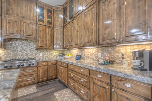 kitchen featuring backsplash, dark wood-style floors, glass insert cabinets, light stone countertops, and stainless steel gas cooktop