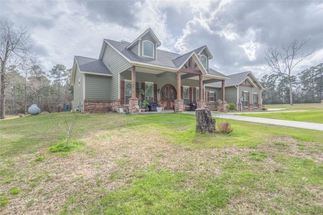 view of front of house with brick siding, covered porch, a front lawn, and roof with shingles