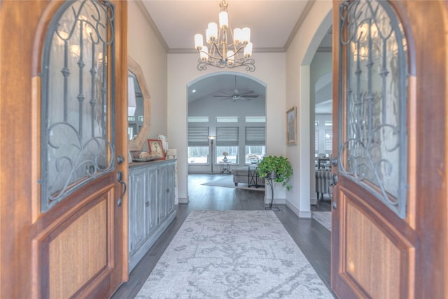 entryway featuring crown molding, dark wood-type flooring, baseboards, ceiling fan with notable chandelier, and arched walkways