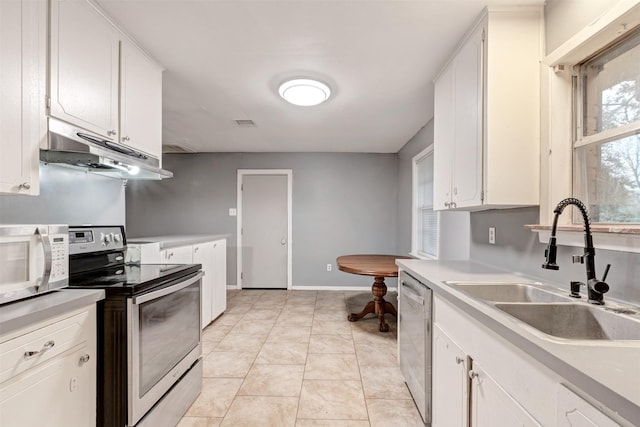 kitchen with light tile patterned flooring, a sink, light countertops, under cabinet range hood, and appliances with stainless steel finishes