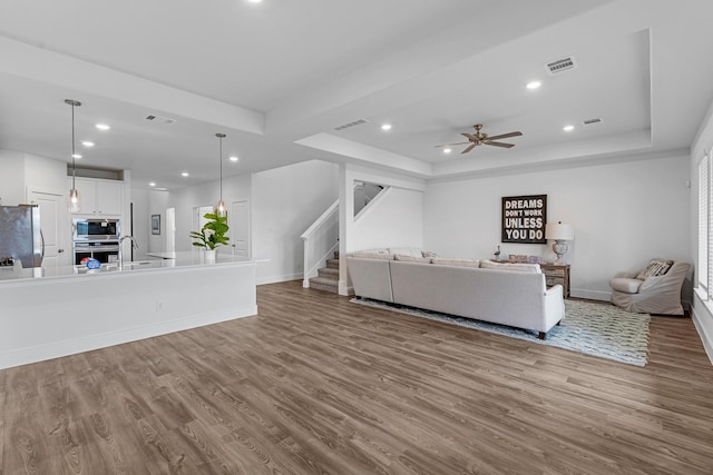 unfurnished living room featuring stairs, a raised ceiling, wood finished floors, and visible vents