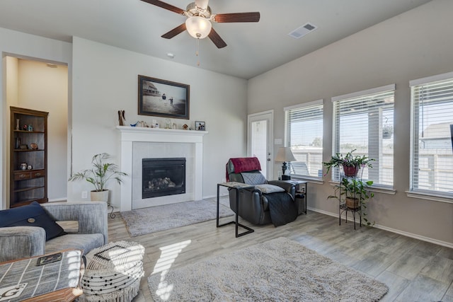 living room featuring visible vents, baseboards, wood finished floors, and a tile fireplace
