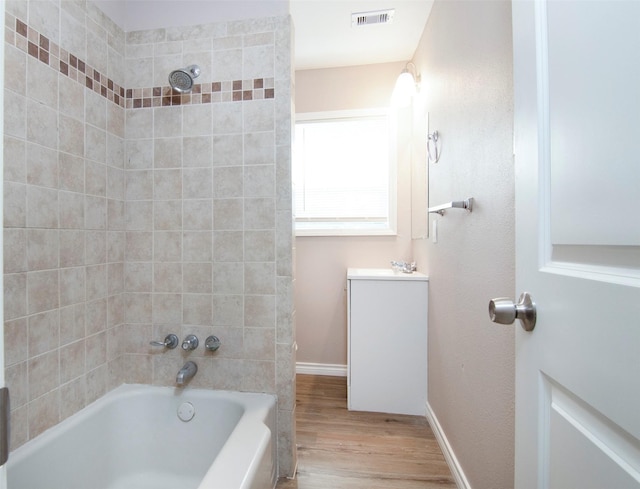 bathroom featuring vanity, wood finished floors, visible vents, baseboards, and shower / washtub combination