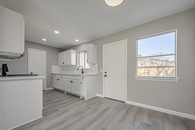 kitchen featuring white cabinetry, light countertops, baseboards, and a sink