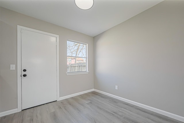 spare room featuring lofted ceiling, baseboards, and light wood-type flooring