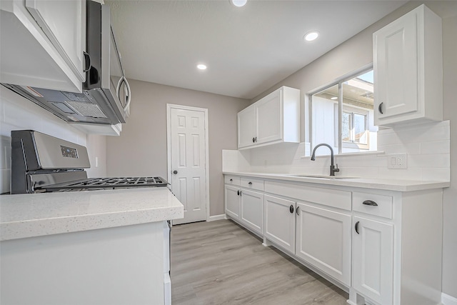 kitchen featuring light wood-style flooring, a sink, appliances with stainless steel finishes, white cabinetry, and tasteful backsplash